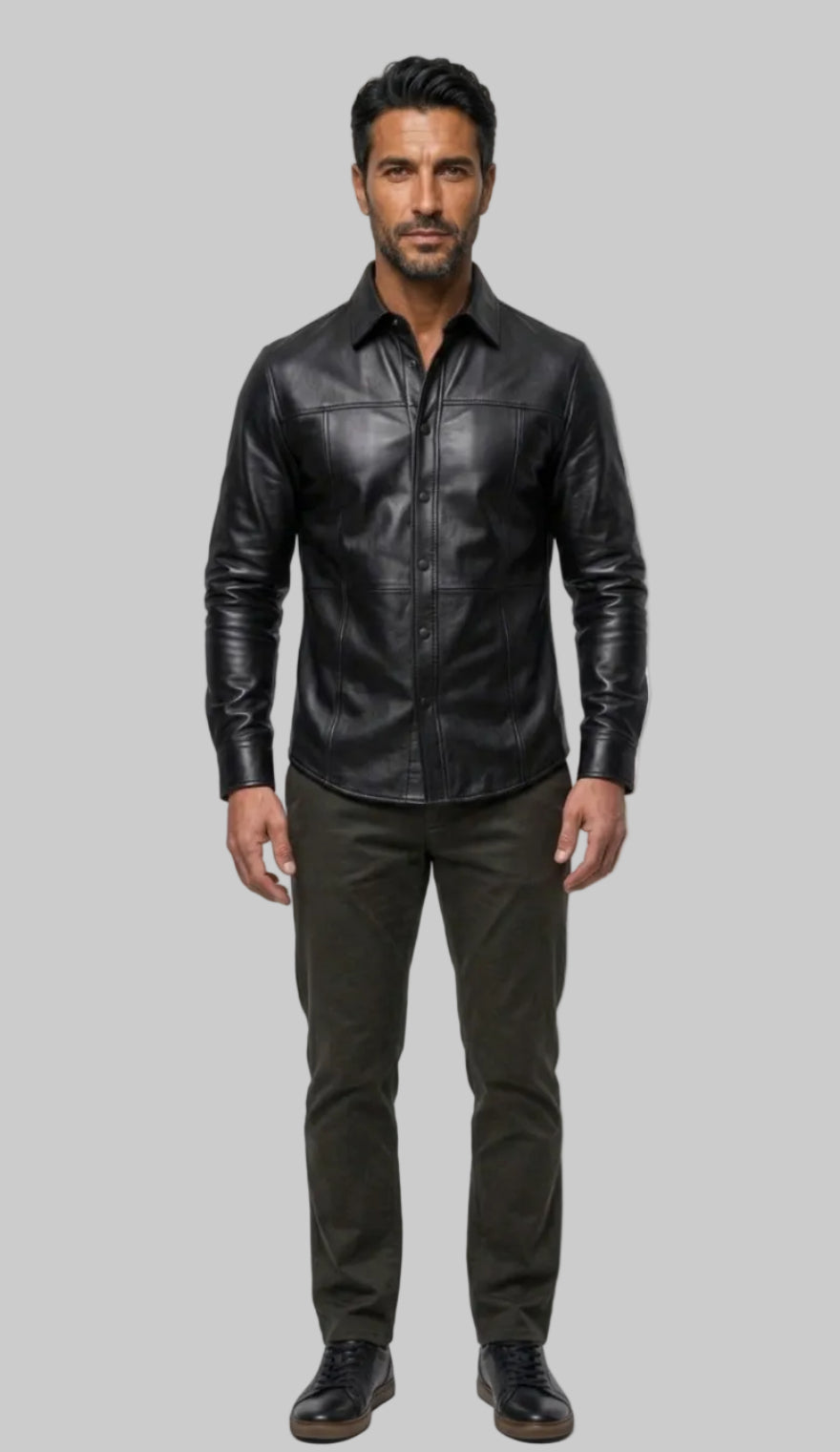 A man modeling our Black Custom Leather Shirt for Men with dark olive pants and black shoes, standing against a off white background.