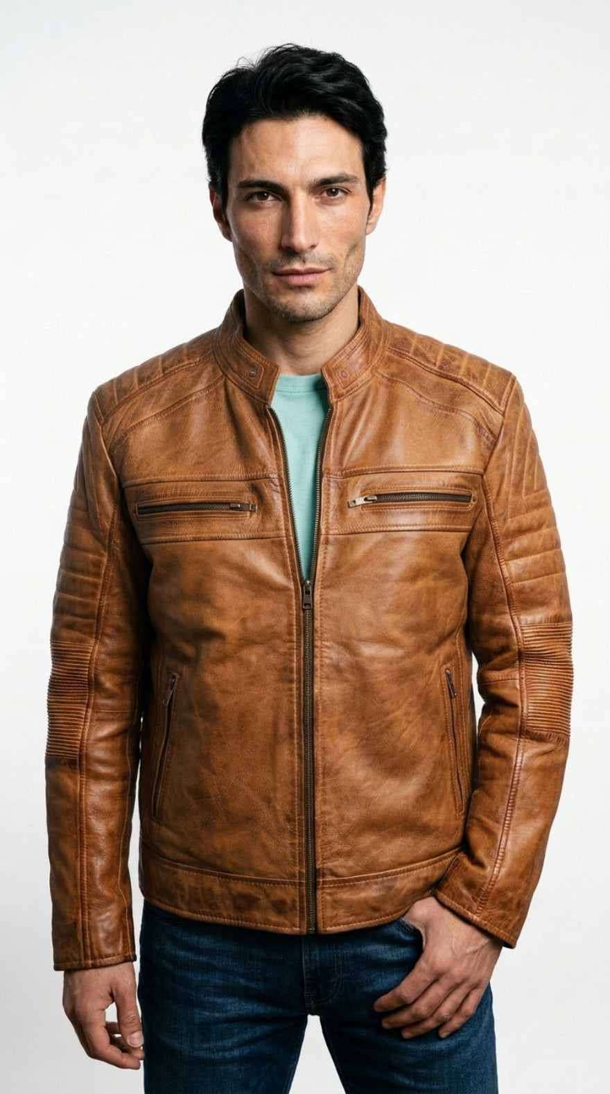 A man wearing a tan cafe racer leather jacket over a light blue t-shirt and dark blue jeans, standing against a plain white studio background.
