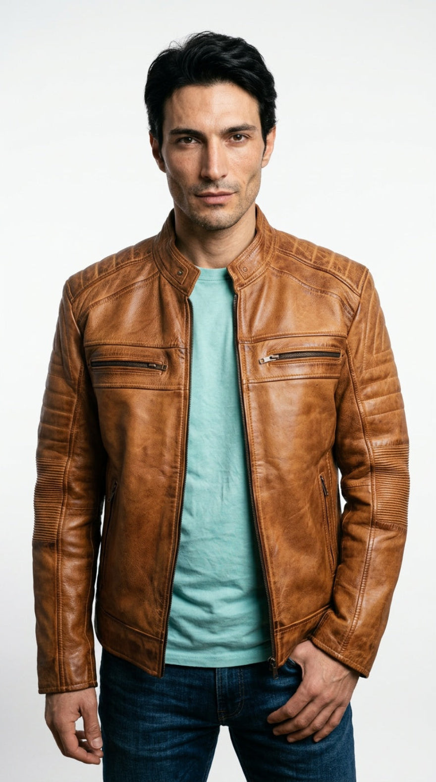 A man wearing a tan cafe racer leather  jacket over a light blue t-shirt and dark blue jeans, standing against a plain white studio background.