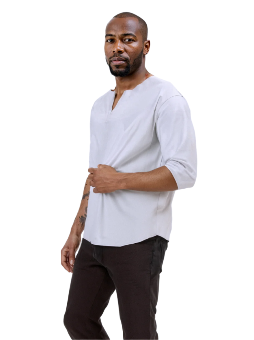 Man wearing a white short-sleeve leather tee shirt and dark pants against a white  background, side view.